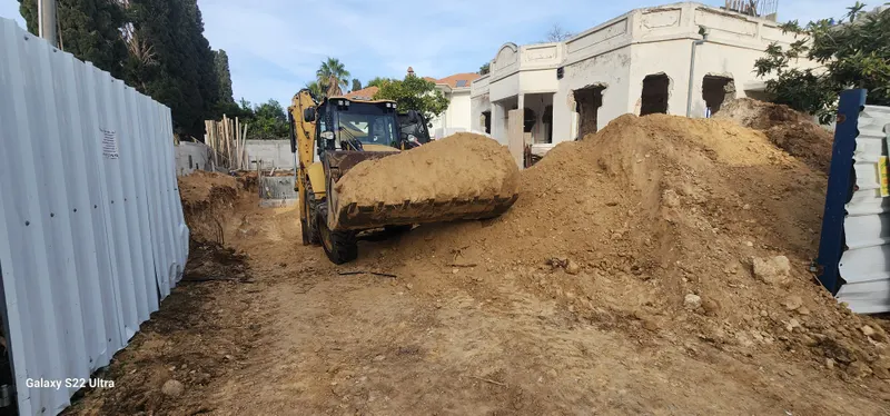 מחפר בעבודות מילוי ופיתוח שטח לצד קיר תוחם